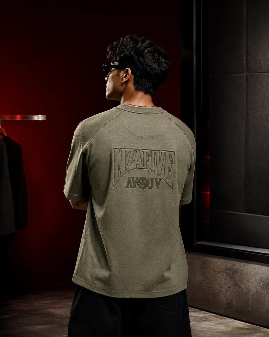 Model wearing an olive tee with tonal embossed back artwork